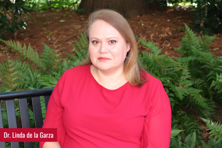 Dr. Garza sitting on a bench on a smile, greenery surrounds her