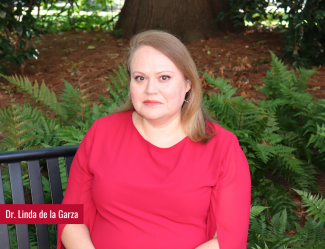 Dr. Garza sitting on a bench on a smile, greenery surrounds her