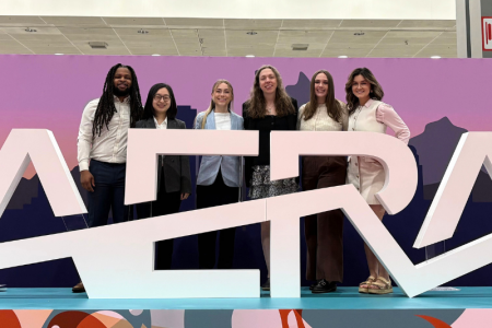 Group of doctoral students post behind a large sign that says AERA.