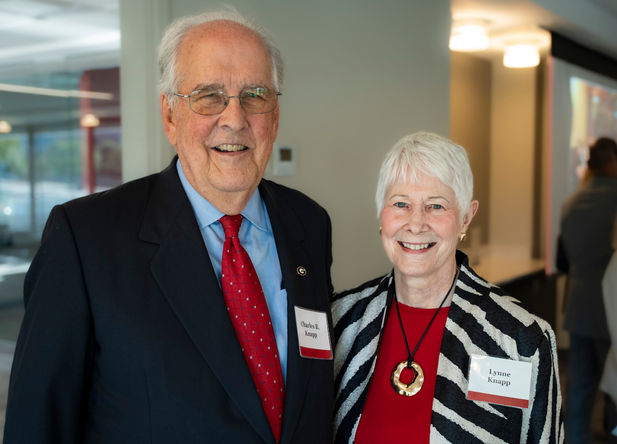 Dr. Charles B. Knapp stands in a black blazer, blue button up shirt, and red tie next to his wife Lynne Knapp, who wears a black and white striped coat over a red blouse.